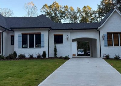 A white brick house with black windows and a driveway leading to an archway with a van parked behind it.
