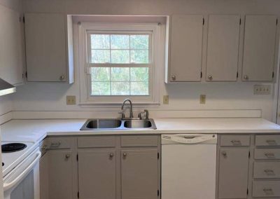A kitchen with gray cabinets, a double sink, a dishwasher, and a window above the sink.