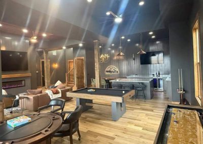 Modern game room with pool table, poker table, bar, shuffleboard, lounge area, and wood flooring.