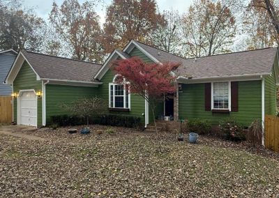 Green house with brown shutters, autumn trees, a red-leafed tree, and fallen leaves covering the yard.