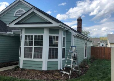Light blue house with white trim, a bay window, and a ladder set up outside on a grassy lawn.