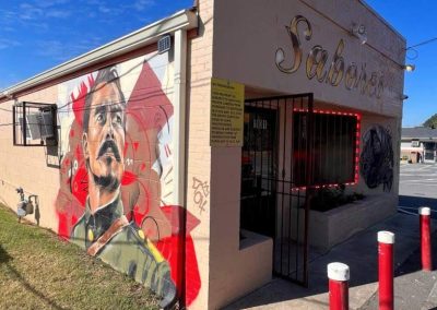 A mural of a man’s face on the side of a tan building with “Sabrosos” written in script above the entrance.