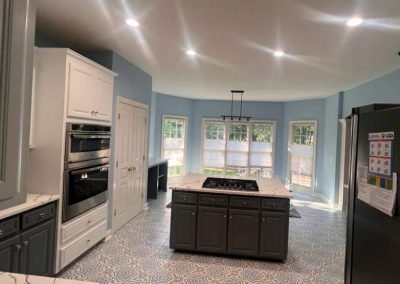 Bright kitchen with blue walls, patterned floor, central island, white cabinets, and large windows with curtains.