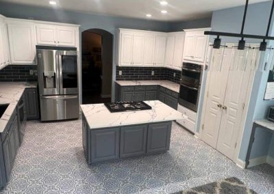 Modern kitchen with gray and white cabinets, marble countertops, stainless steel appliances, and patterned floor tiles.