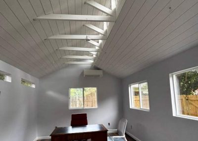 Modern office with wood floors, white walls, high slanted ceiling, and large windows letting in natural light.