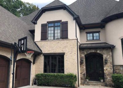 A two-story house with brick and stone exterior, arched door, garage, and a basketball hoop in the driveway.