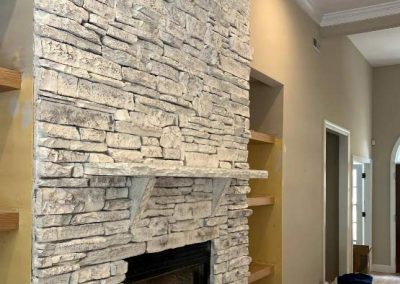 Stone fireplace with a mantel, built-in shelves on the left, and a hardwood floor in a living room.
