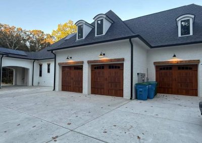 Large house with three wooden garage doors, two blue recycling bins, and a white van parked on a concrete driveway.
