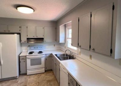 Kitchen with white cabinets, white appliances, double sink, window above sink, and beige tile floor.