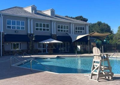 Outdoor swimming pool with a lifeguard chair, surrounded by a building and trees on a sunny day.