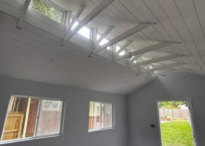 Bright room with vaulted ceiling, exposed beams, large windows, and an open door leading to a green backyard.