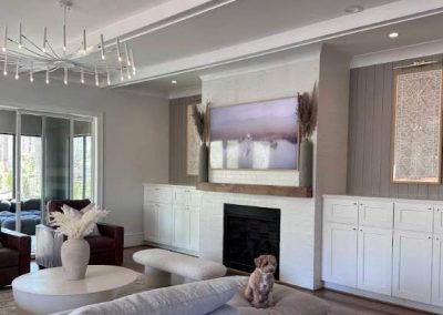Modern living room with a gray sofa, round table, fireplace, and a small dog sitting on the sofa.