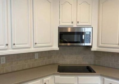 White kitchen cabinets with a built-in microwave above a stovetop and beige tiled backsplash.