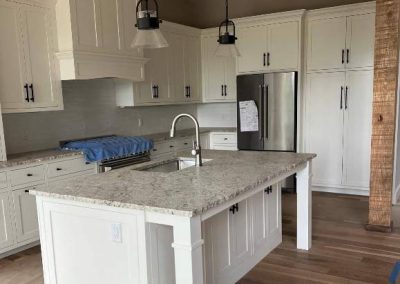 Modern kitchen with white cabinets, a granite island, pendant lights, and stainless steel appliances.